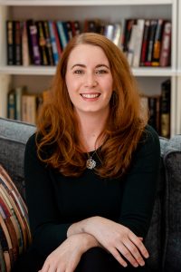 headshot of author Freya Marske sitting on couch in front of bookshelf