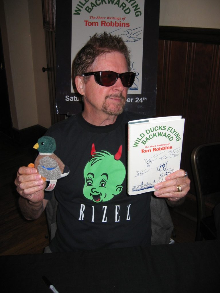 Tom Robbins holding a stuffed duck toy and his book